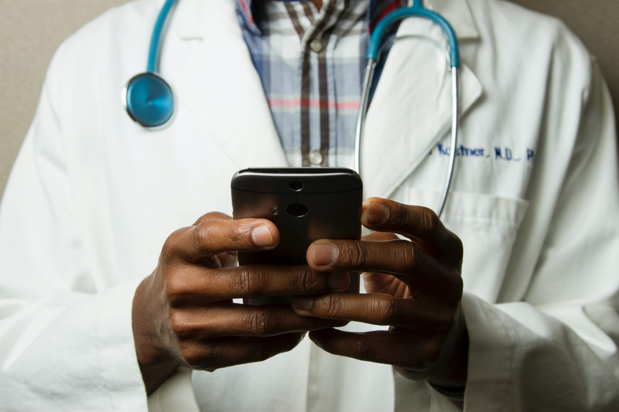 doctor in lab coat with stehescope on cell phone